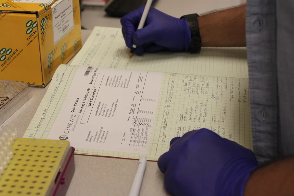 Gloved hands recording sample details on a laboratory record sheet